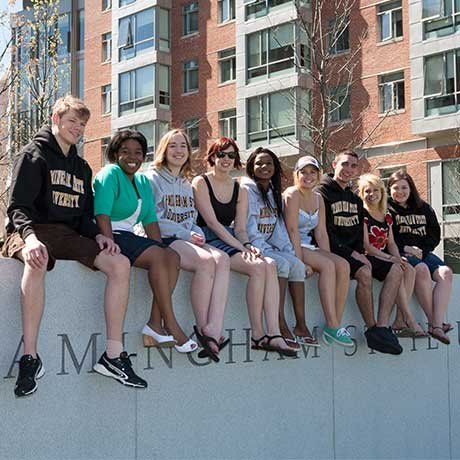 Group of students sitting on a wall that reads, "Framingham State University"